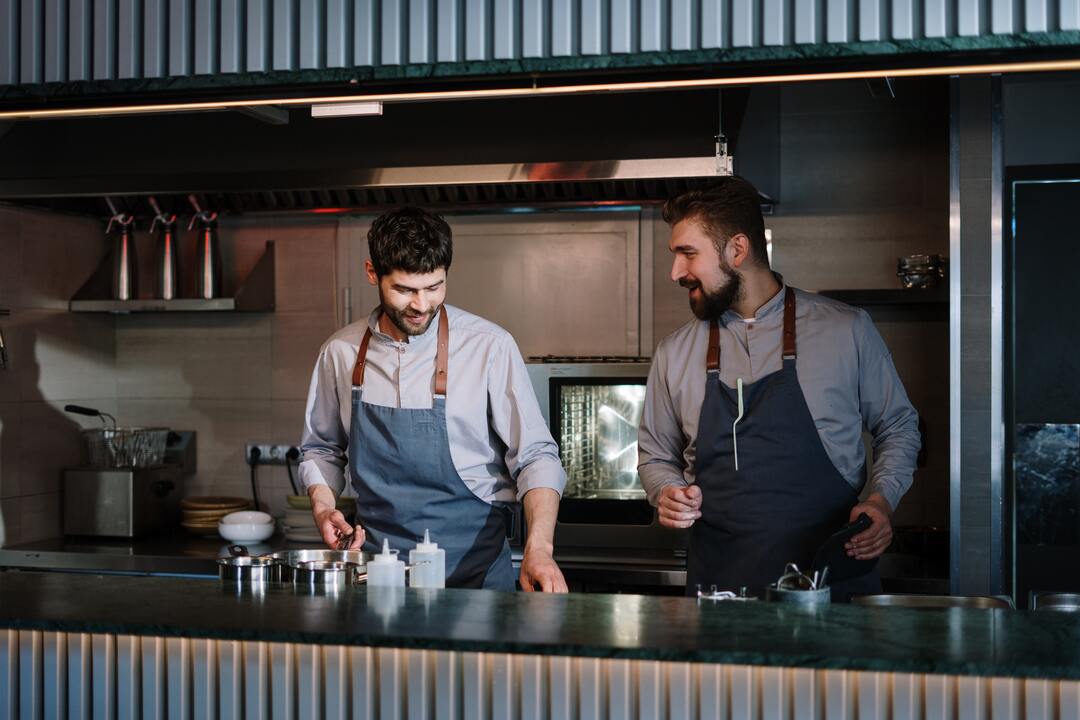 Man in Black Vest and White Dress Shirt Standing Beside Man in Black Vest men working in kitchen