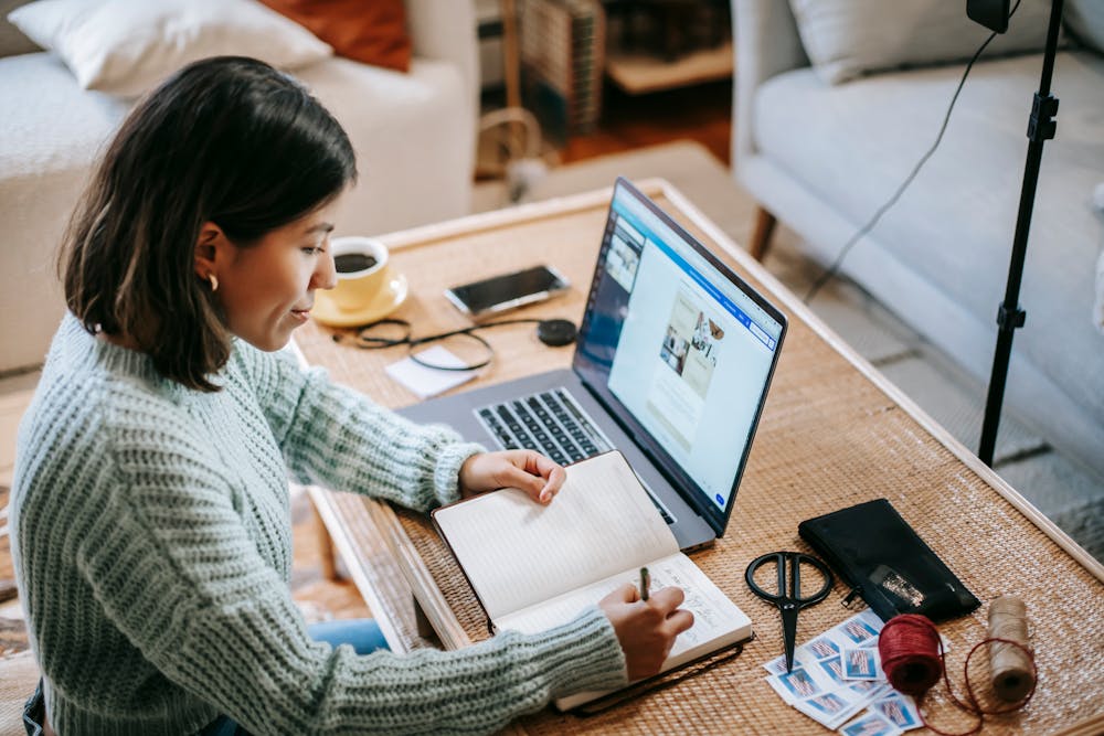 Young focused woman writing in planner while using laptop Young focused woman writing in planner while using laptop